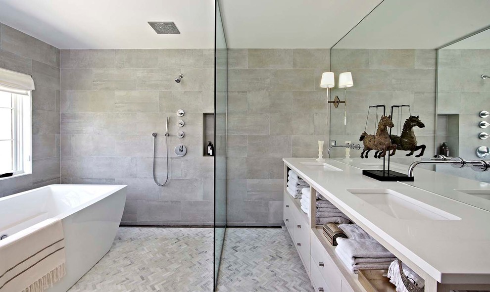 This is an example of a large modern master bathroom in New York with flat-panel cabinets, beige cabinets, a freestanding tub, an open shower, beige tile, ceramic tile, grey walls, concrete floors, an undermount sink and solid surface benchtops.