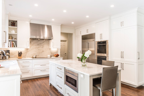Kitchen cabinet design in bright white Shaker style with full-height pantry units, stainless range hood, built-in fridge and double ovens, stone-slab backsplash, and a large island with microwave and seating.