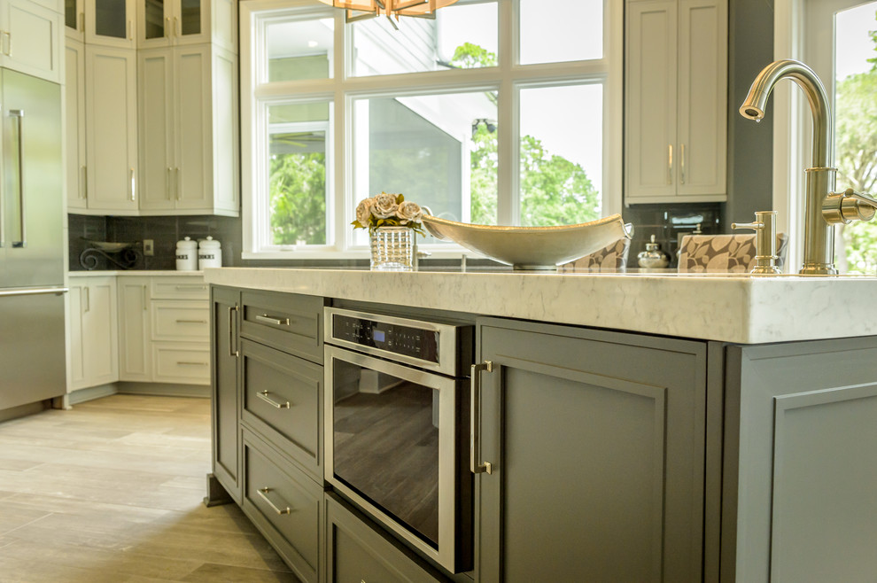 Mid-sized transitional u-shaped eat-in kitchen in Charleston with a farmhouse sink, shaker cabinets, grey cabinets, stainless steel appliances, porcelain floors, with island, brown floor, glass tile splashback, grey splashback and quartz benchtops.