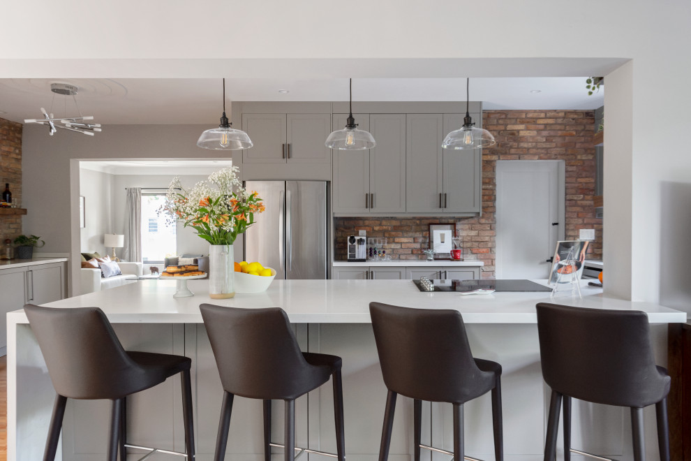 Inspiration for a mid-sized transitional galley medium tone wood floor eat-in kitchen remodel in Miami with an undermount sink, shaker cabinets, gray cabinets, quartz countertops, white backsplash, subway tile backsplash, stainless steel appliances, a peninsula and white countertops