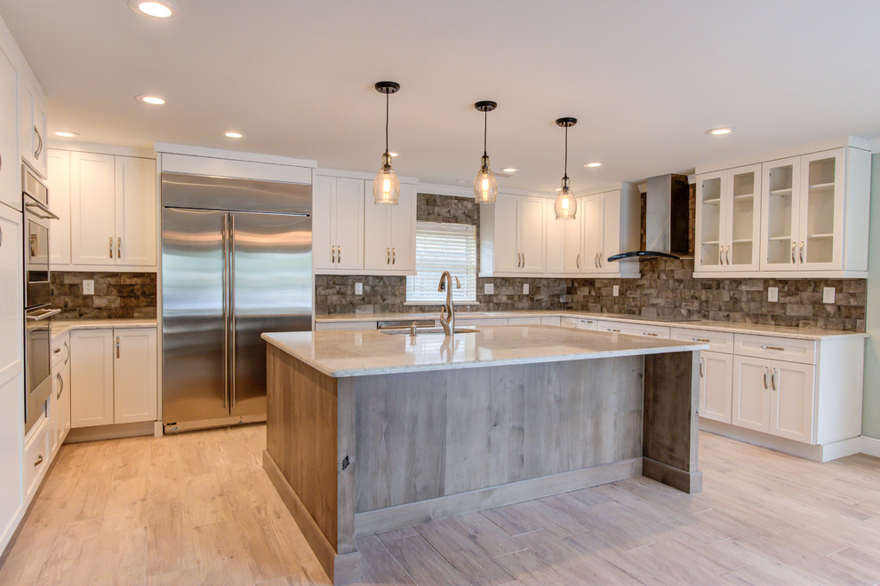 Large transitional u-shaped porcelain tile and brown floor enclosed kitchen photo with an undermount sink, shaker cabinets, white cabinets, quartz countertops, brown backsplash, stainless steel appliances, an island and beige countertops