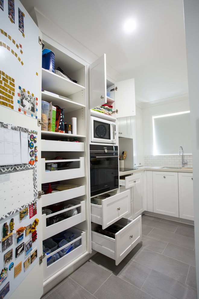 This is an example of a small traditional u-shaped kitchen pantry in Brisbane with a double-bowl sink, shaker cabinets, white cabinets, quartz benchtops, grey splashback, ceramic splashback, black appliances, porcelain floors, with island, grey floor and white benchtop.