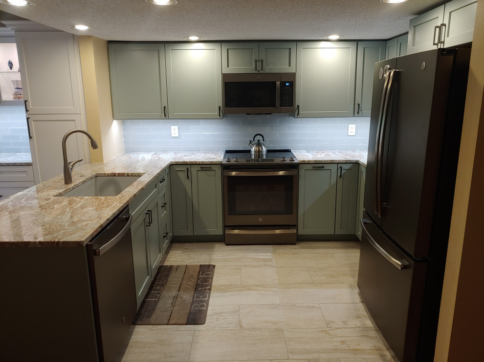 Photo of a mid-sized transitional u-shaped eat-in kitchen in Tampa with an undermount sink, shaker cabinets, green cabinets, granite benchtops, white splashback, glass tile splashback, stainless steel appliances, ceramic floors, a peninsula, beige floor and brown benchtop.