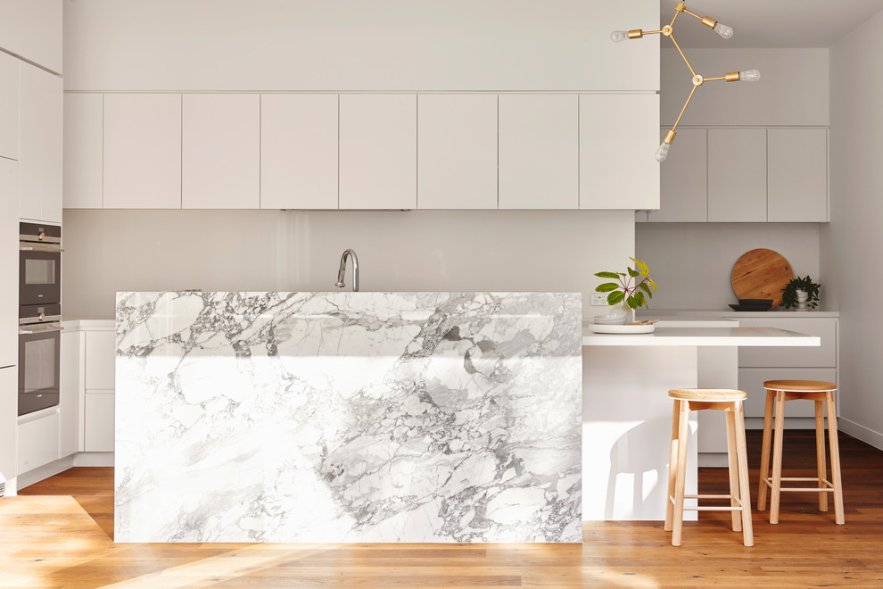 Inspiration for a contemporary l-shaped kitchen in Geelong with white cabinets, marble benchtops, with island, flat-panel cabinets, stainless steel appliances, medium hardwood floors, brown floor and white benchtop.