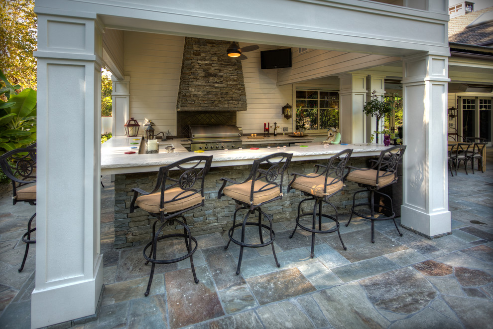 Design ideas for an expansive traditional backyard patio in Orange County with an outdoor kitchen, natural stone pavers and a roof extension.