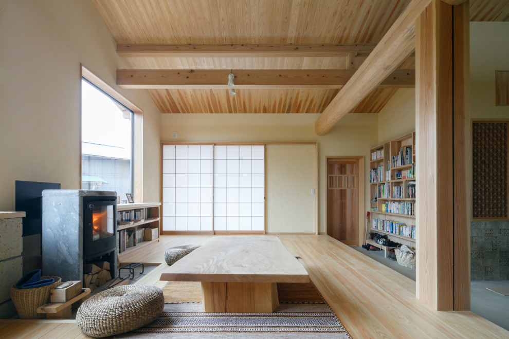 Modelo de comedor de estilo zen con suelo de madera en tonos medios, estufa de leña, marco de chimenea de piedra y vigas vistas
