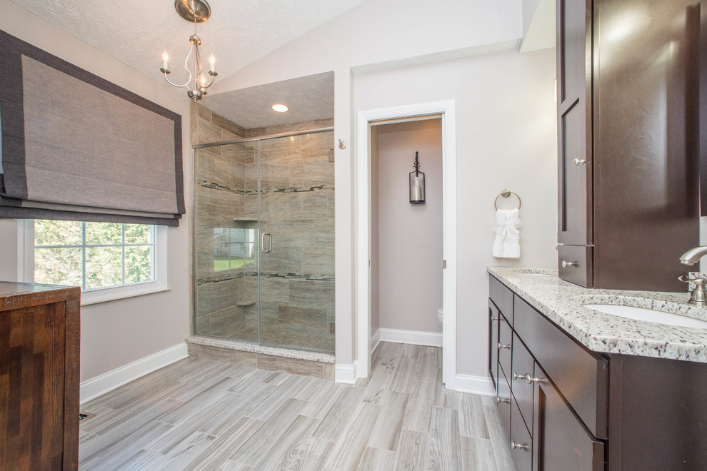 Design ideas for a mid-sized transitional master bathroom in Other with shaker cabinets, dark wood cabinets, an alcove shower, a two-piece toilet, beige tile, brown tile, porcelain tile, grey walls, porcelain floors, an undermount sink, granite benchtops, grey floor and a hinged shower door.
