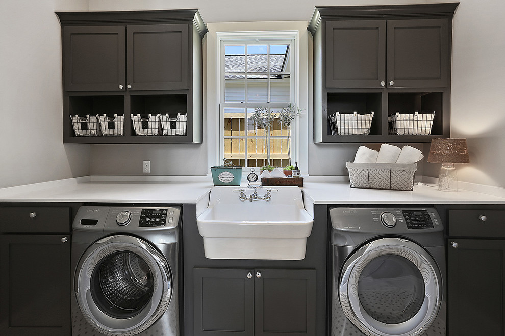 Inspiration for a large transitional single-wall utility room in New Orleans with a farmhouse sink, recessed-panel cabinets, grey cabinets, grey walls, a side-by-side washer and dryer, quartz benchtops and white benchtop.