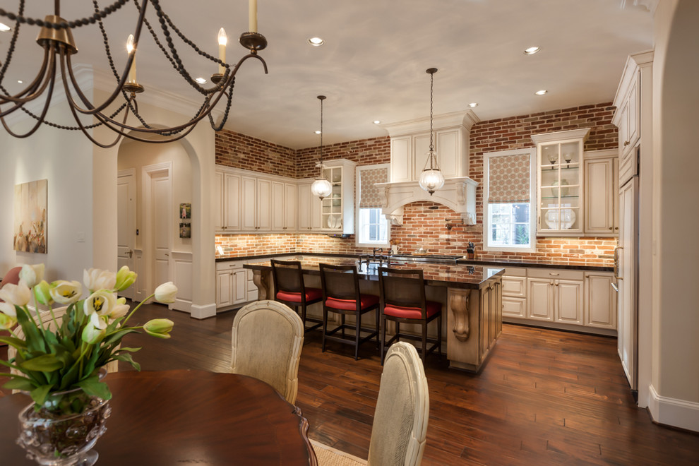 Large transitional u-shaped medium tone wood floor open concept kitchen photo in Houston with a farmhouse sink, raised-panel cabinets, white cabinets, granite countertops, multicolored backsplash, terra-cotta backsplash, paneled appliances and an island
