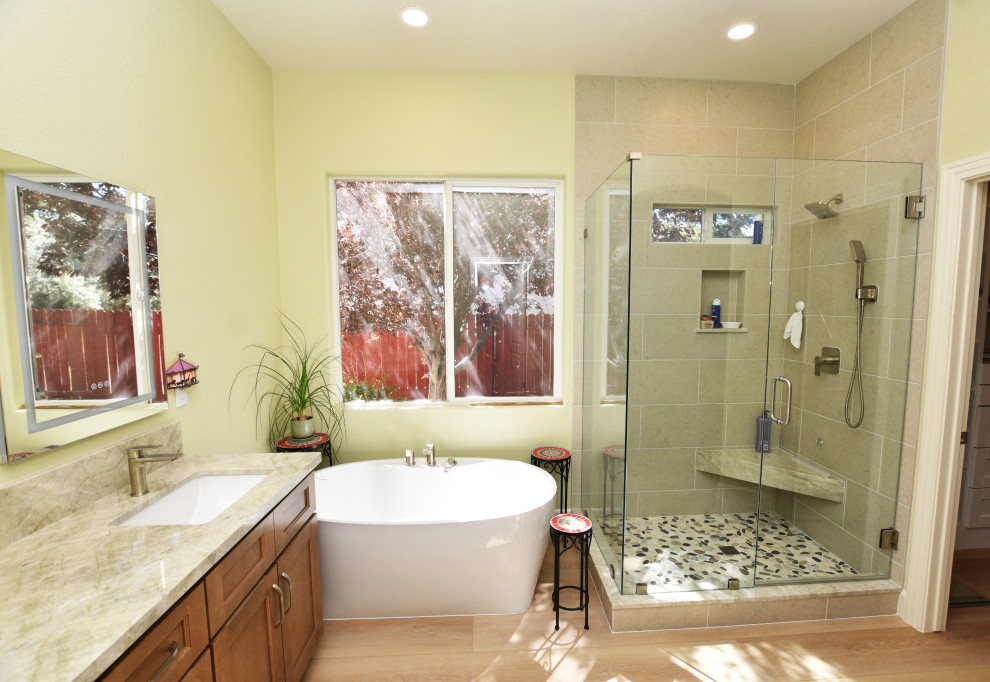 Example of a large transitional master gray tile and porcelain tile vinyl floor, beige floor and double-sink corner shower design with shaker cabinets, medium tone wood cabinets, a two-piece toilet, green walls, an undermount sink, quartzite countertops, a hinged shower door, beige countertops and a built-in vanity