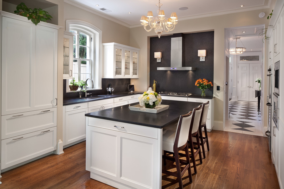 Inspiration for a mid-sized traditional l-shaped eat-in kitchen in DC Metro with recessed-panel cabinets, white cabinets, black splashback, panelled appliances, stone slab splashback, an undermount sink, limestone benchtops, medium hardwood floors and with island.