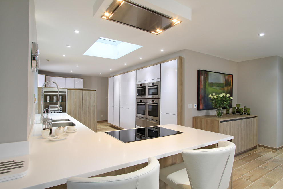 Design ideas for an expansive contemporary u-shaped open plan kitchen in Hampshire with an integrated sink, flat-panel cabinets, medium wood cabinets, white splashback, stainless steel appliances, ceramic floors and a peninsula.