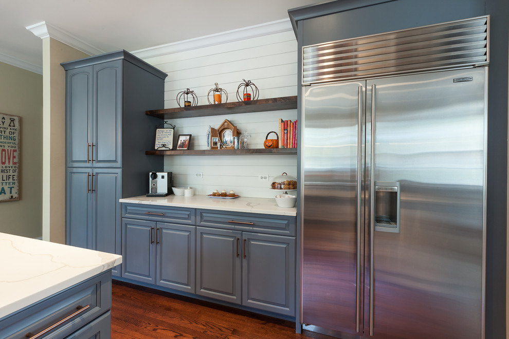 Inspiration for a large country u-shaped eat-in kitchen in Chicago with a farmhouse sink, raised-panel cabinets, blue cabinets, quartz benchtops, beige splashback, porcelain splashback, stainless steel appliances, medium hardwood floors, with island and brown floor.