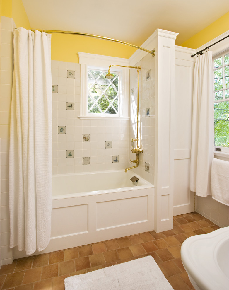 This is an example of a mid-sized traditional kids bathroom in New York with a pedestal sink, white cabinets, marble benchtops, a drop-in tub, a shower/bathtub combo, a one-piece toilet, multi-coloured tile, yellow walls, terra-cotta floors and recessed-panel cabinets.