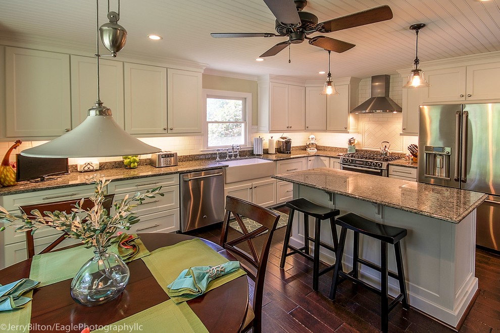 Example of a large transitional l-shaped dark wood floor and brown floor eat-in kitchen design with a farmhouse sink, shaker cabinets, white cabinets, granite countertops, white backsplash, subway tile backsplash, stainless steel appliances and an island