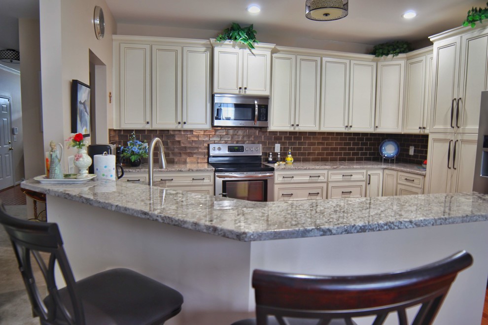 Mid-sized u-shaped medium tone wood floor and brown floor kitchen photo in Charleston with an undermount sink, raised-panel cabinets, beige cabinets, granite countertops, brown backsplash, ceramic backsplash, stainless steel appliances and beige countertops