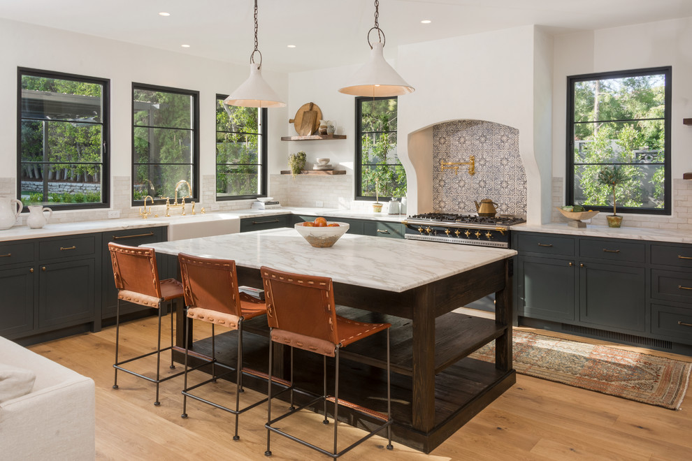 Mediterranean l-shaped kitchen in Los Angeles with shaker cabinets, with island, a farmhouse sink, multi-coloured splashback, black appliances, light hardwood floors, multi-coloured benchtop and green cabinets.