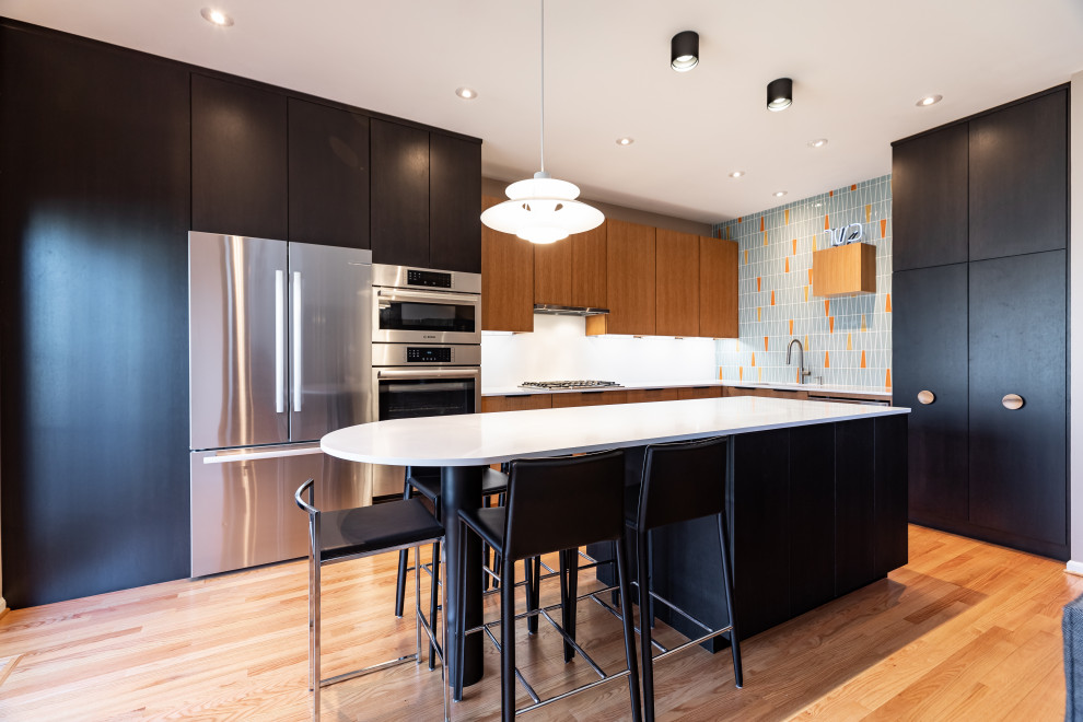 Example of a mid-sized trendy l-shaped light wood floor and brown floor open concept kitchen design in Philadelphia with an undermount sink, flat-panel cabinets, brown cabinets, quartz countertops, white backsplash, porcelain backsplash, stainless steel appliances, an island and white countertops