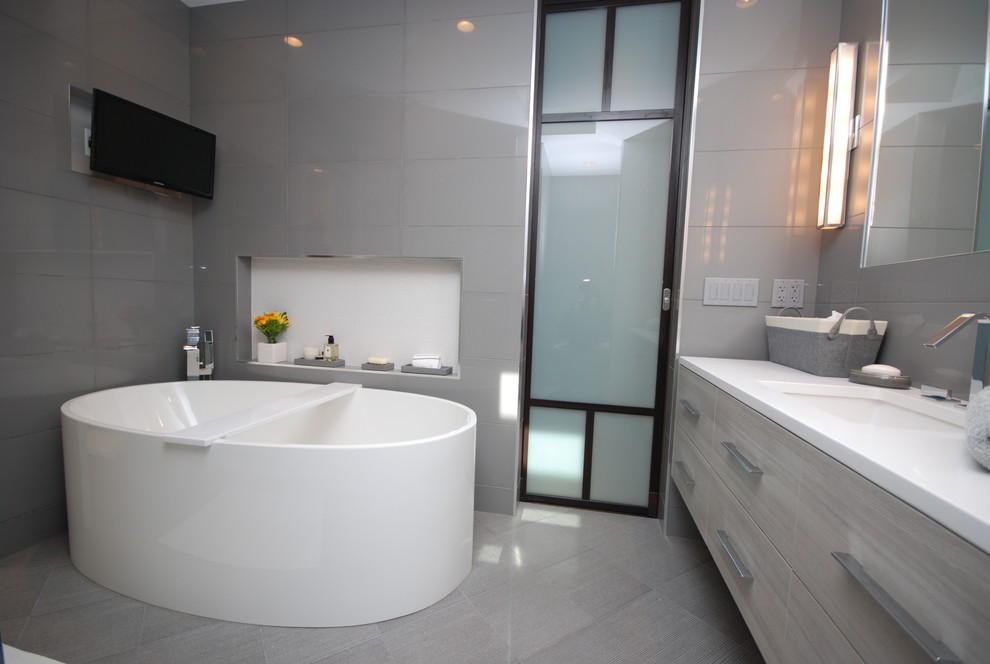 Inspiration for a mid-sized contemporary master bathroom in Chicago with flat-panel cabinets, grey cabinets, a freestanding tub, an alcove shower, gray tile, glass tile, grey walls, porcelain floors, an undermount sink, solid surface benchtops, grey floor and a hinged shower door.