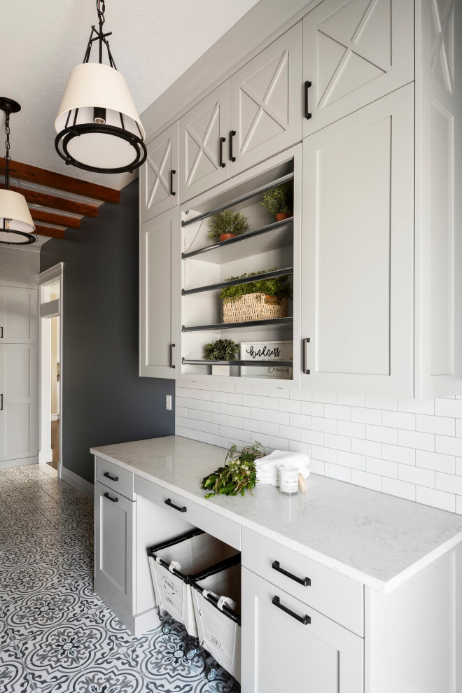 Photo of a traditional galley dedicated laundry room with a drop-in sink, shaker cabinets, grey cabinets, quartz benchtops, white splashback, subway tile splashback, blue walls, porcelain floors, a side-by-side washer and dryer, multi-coloured floor, white benchtop and exposed beam.