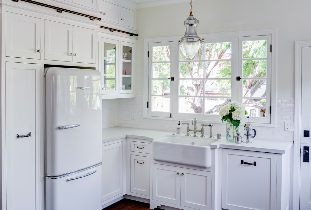 Mid-sized transitional u-shaped eat-in kitchen in Los Angeles with a farmhouse sink, shaker cabinets, white cabinets, solid surface benchtops, white splashback, subway tile splashback, stainless steel appliances, medium hardwood floors and a peninsula.