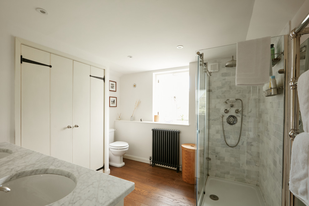 Inspiration for a traditional kids bathroom in Cornwall with grey cabinets, an open shower, a one-piece toilet, white walls, medium hardwood floors, a drop-in sink, marble benchtops, brown floor, grey benchtops, a double vanity and a built-in vanity.