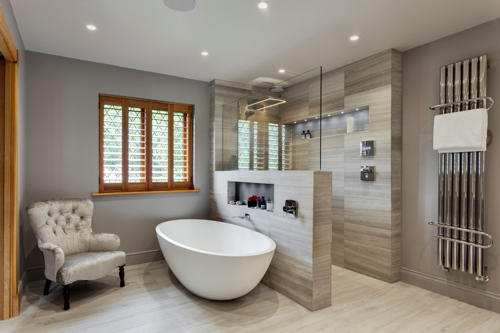 Inredning av ett klassiskt stort en-suite badrum, med skåp i ljust trä, ett fristående badkar, en öppen dusch, grå kakel, stenhäll, grå väggar, kalkstensgolv, ett nedsänkt handfat och marmorbänkskiva