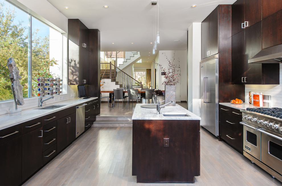 Design ideas for a large contemporary u-shaped kitchen in Seattle with flat-panel cabinets, dark wood cabinets, white splashback, stainless steel appliances, light hardwood floors and with island.