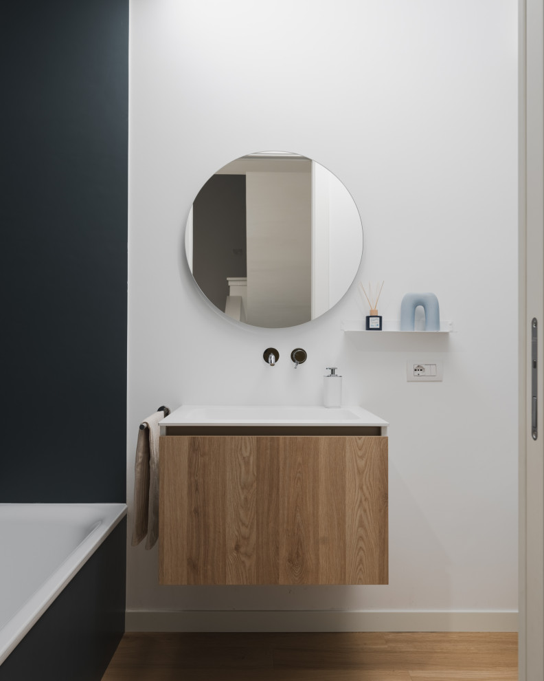 Design ideas for a small scandinavian bathroom in Milan with flat-panel cabinets, light wood cabinets, an alcove tub, a two-piece toilet, blue tile, porcelain tile, white walls, light hardwood floors, an integrated sink, solid surface benchtops, beige floor, white benchtops, a niche, a single vanity and a floating vanity.
