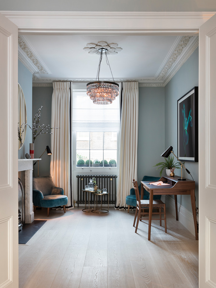 Inspiration for a mid-sized transitional study room in London with blue walls, light hardwood floors, a standard fireplace, a stone fireplace surround, a freestanding desk and beige floor.