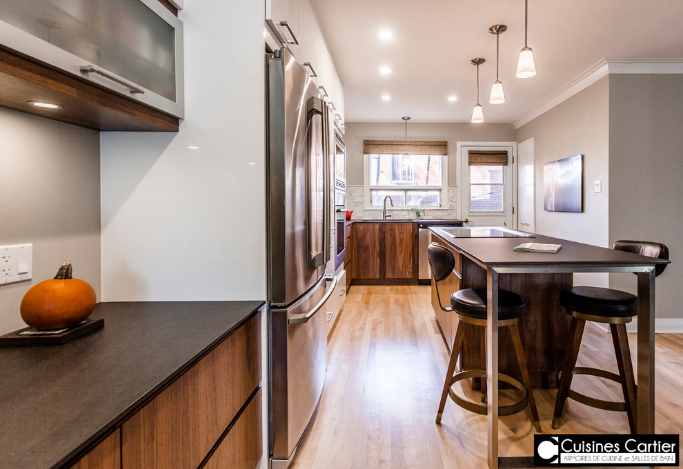 Large transitional galley medium tone wood floor eat-in kitchen photo in Montreal with an undermount sink, flat-panel cabinets, dark wood cabinets, quartzite countertops, white backsplash, mosaic tile backsplash, stainless steel appliances and an island