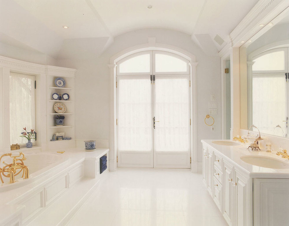 Photo of a large traditional master bathroom in Montreal with raised-panel cabinets, white cabinets, a drop-in tub, white walls, an undermount sink and solid surface benchtops.