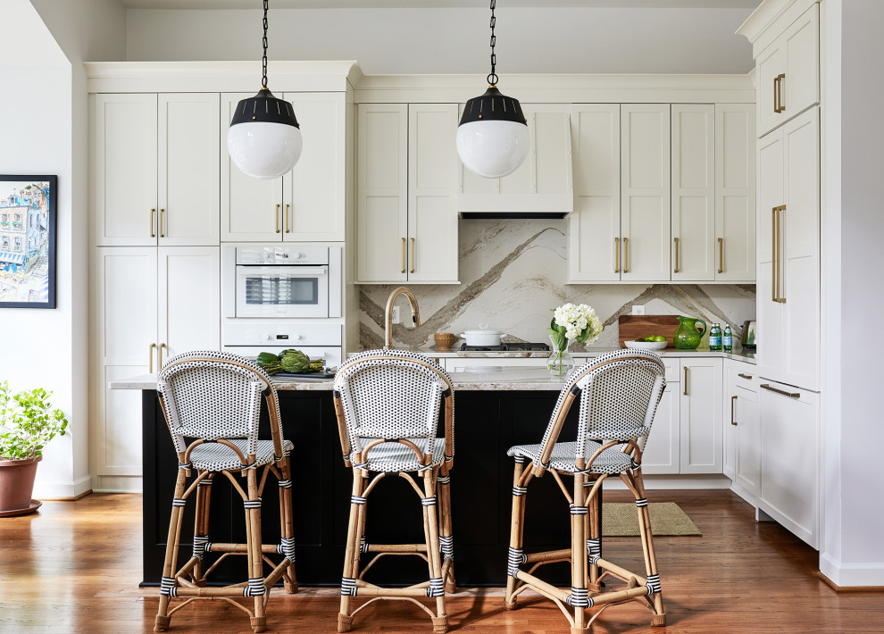 Inspiration for a mid-sized transitional l-shaped open plan kitchen in Chicago with a farmhouse sink, recessed-panel cabinets, white cabinets, quartz benchtops, white splashback, engineered quartz splashback, white appliances, medium hardwood floors, with island, brown floor and white benchtop.