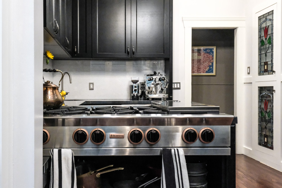 Mid-sized victorian u-shaped separate kitchen in San Francisco with an undermount sink, shaker cabinets, black cabinets, quartz benchtops, white splashback, ceramic splashback, stainless steel appliances, dark hardwood floors, with island, brown floor and black benchtop.