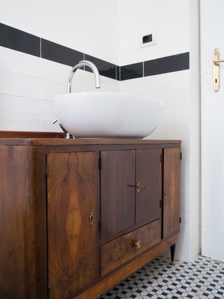 This is an example of a small midcentury 3/4 bathroom in Other with furniture-like cabinets, dark wood cabinets, an alcove shower, a wall-mount toilet, white tile, ceramic tile, white walls, porcelain floors, a vessel sink, wood benchtops, black floor and brown benchtops.