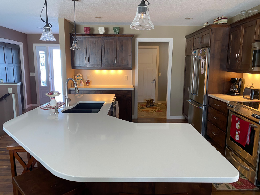 Medium sized classic u-shaped kitchen/diner in Minneapolis with a double-bowl sink, dark wood cabinets, engineered stone countertops, white splashback, stainless steel appliances, dark hardwood flooring, an island, brown floors and white worktops.