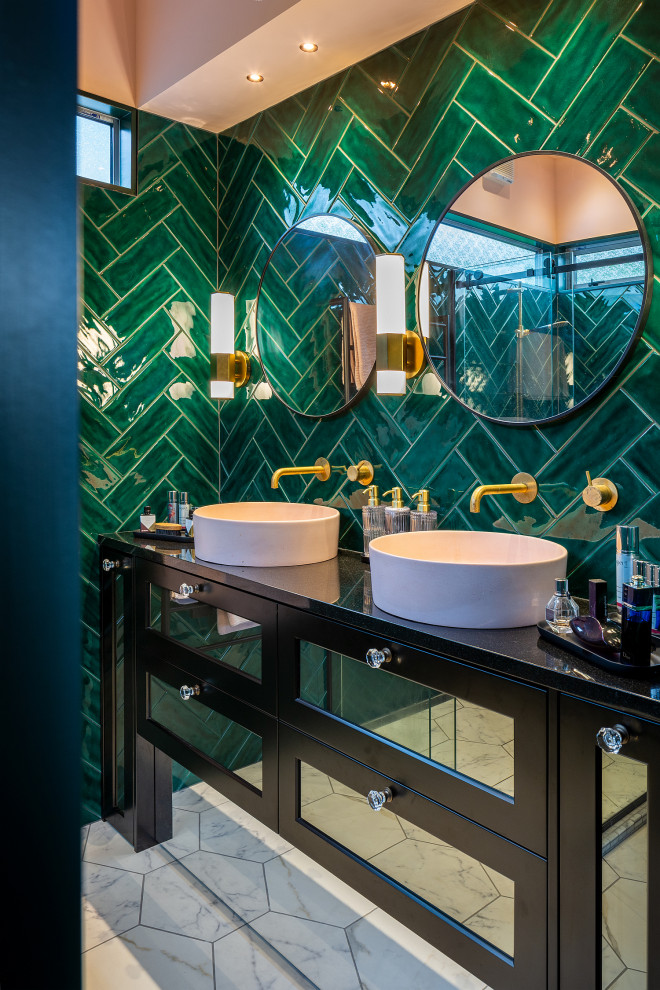 Photo of a small world-inspired ensuite bathroom in Wellington with glass-front cabinets, brown cabinets, a corner shower, a one-piece toilet, green tiles, ceramic tiles, green walls, ceramic flooring, a vessel sink, granite worktops, white floors, a sliding door, black worktops, double sinks and a built in vanity unit.
