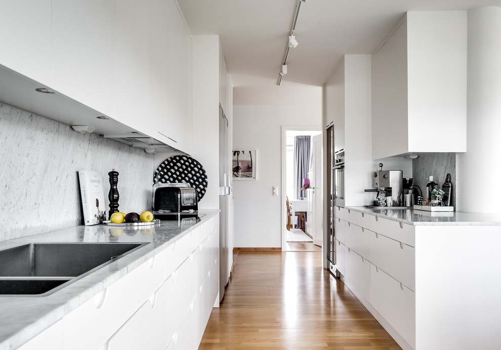 Photo of a mid-sized transitional kitchen in Stockholm with flat-panel cabinets, white cabinets, grey splashback, marble splashback, stainless steel appliances, medium hardwood floors and brown floor.