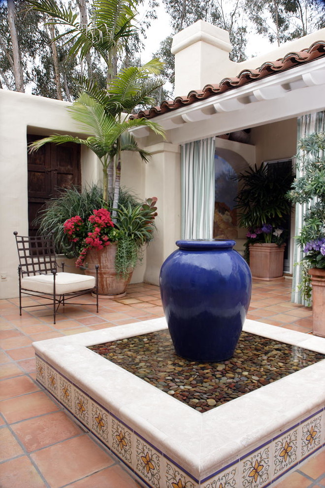 This is an example of a mid-sized mediterranean side yard patio in San Diego with a water feature, tile and no cover.