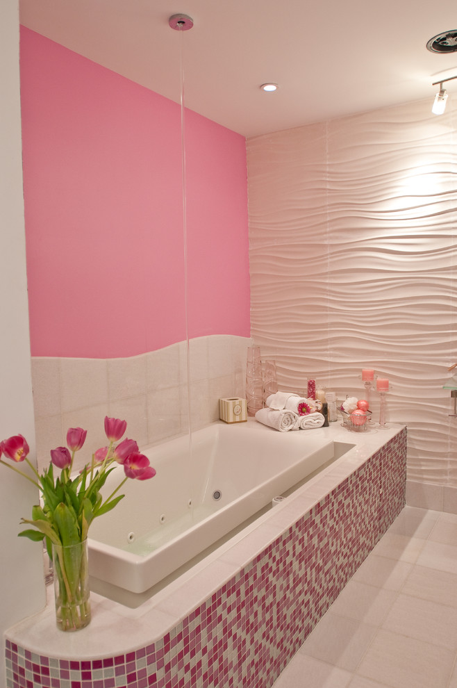 Photo of a large modern kids bathroom in New York with open cabinets, a drop-in tub, a corner shower, a one-piece toilet, pink tile, mosaic tile, pink walls, ceramic floors, a wall-mount sink, glass benchtops and white floor.