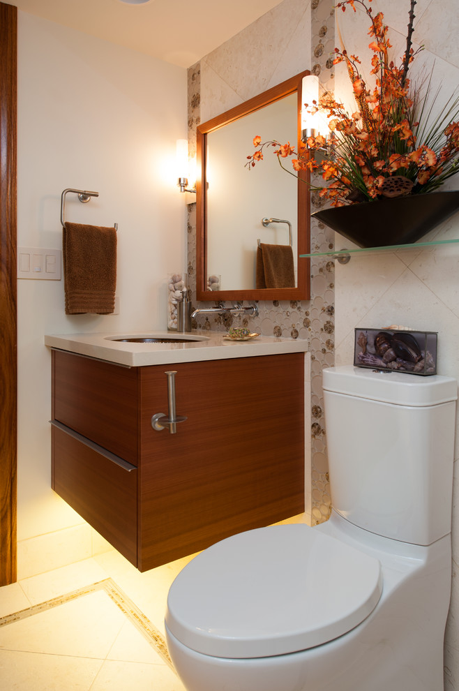 Inspiration for a tropical bathroom in Hawaii with flat-panel cabinets, medium wood cabinets, a two-piece toilet, white tile, glass tile, beige walls, limestone floors, an undermount sink and engineered quartz benchtops.
