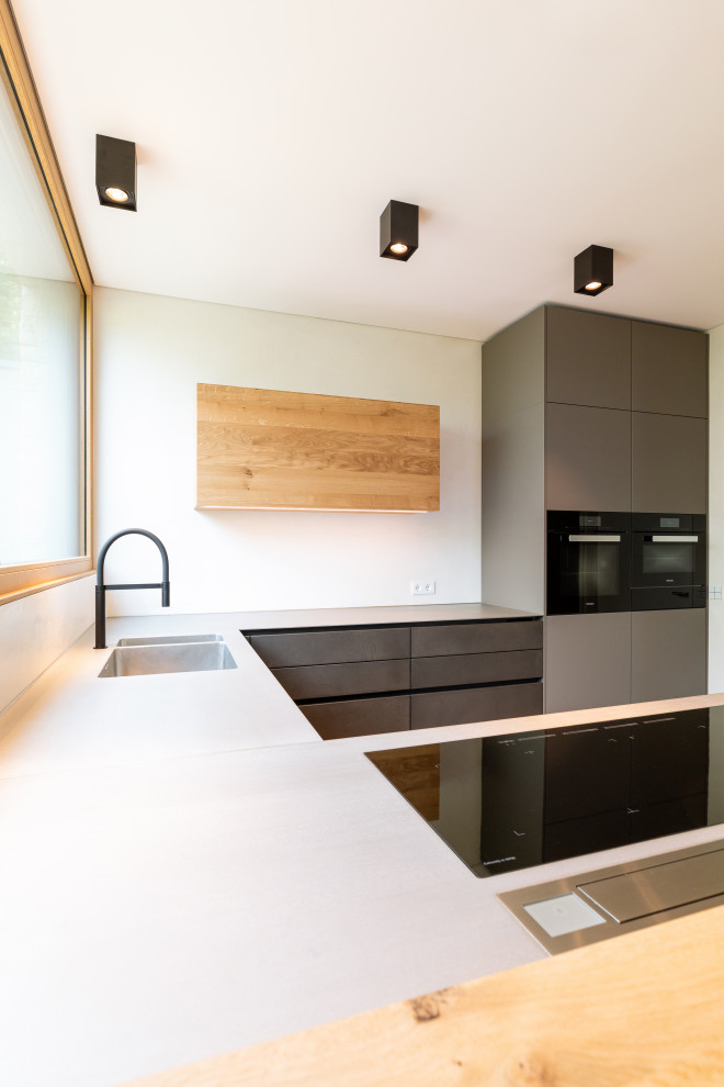 Offene, Mittelgroße Moderne Küche in U-Form mit integriertem Waschbecken, flächenbündigen Schrankfronten, grauen Schränken, Edelstahl-Arbeitsplatte, schwarzen Elektrogeräten, hellem Holzboden, Halbinsel, braunem Boden und grauer Arbeitsplatte in Frankfurt am Main