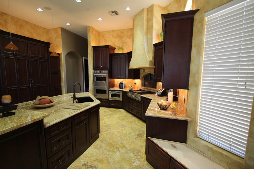 Design ideas for a large transitional l-shaped eat-in kitchen in Phoenix with a double-bowl sink, raised-panel cabinets, dark wood cabinets, granite benchtops, yellow splashback, ceramic splashback, stainless steel appliances, travertine floors and with island.