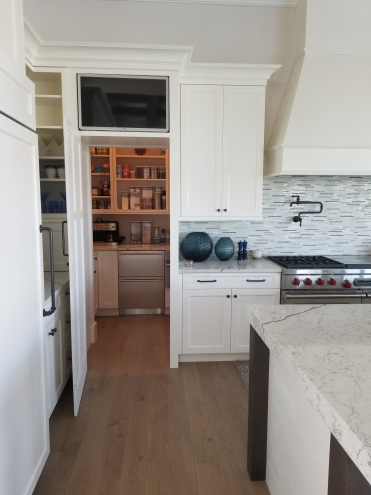 Inspiration for a large transitional kitchen pantry in Miami with a farmhouse sink, shaker cabinets, white cabinets, quartz benchtops, beige splashback, stone tile splashback, panelled appliances, medium hardwood floors, with island, beige floor and multi-coloured benchtop.