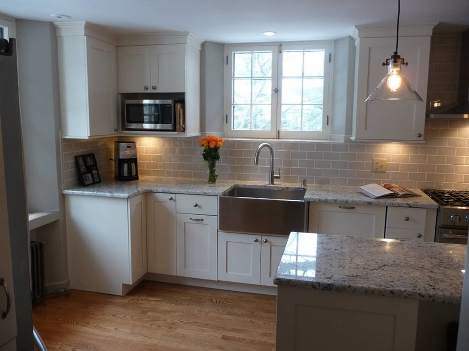 Example of a large transitional u-shaped light wood floor eat-in kitchen design in Milwaukee with a farmhouse sink, recessed-panel cabinets, white cabinets, granite countertops, gray backsplash, subway tile backsplash, stainless steel appliances and an island
