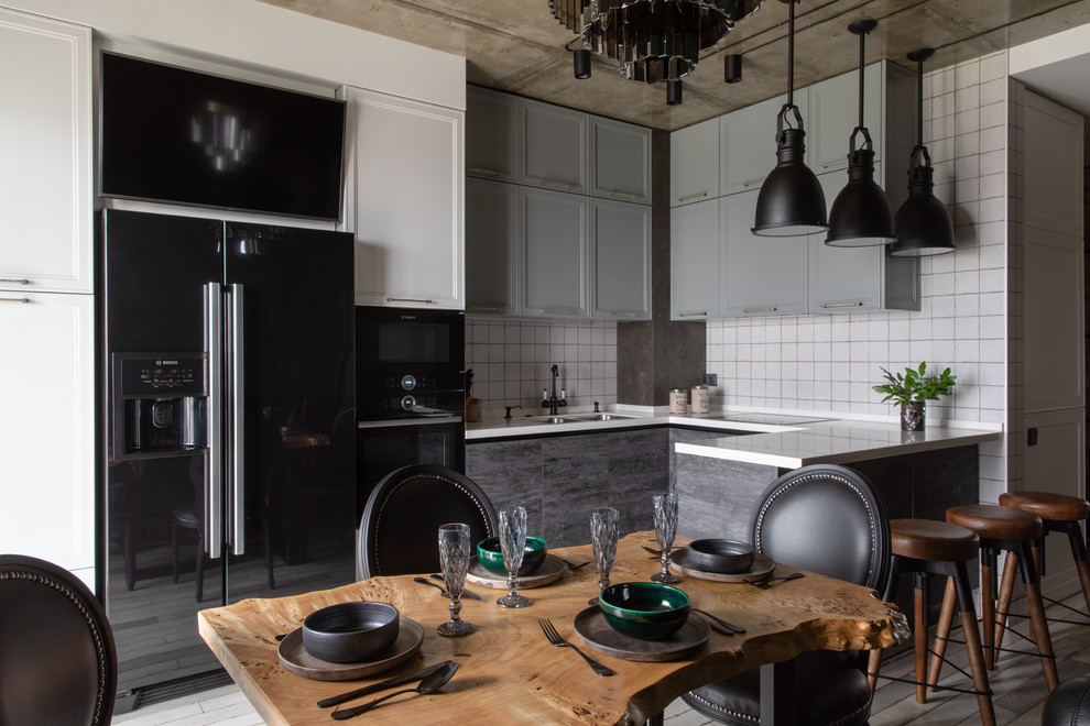This is an example of an industrial u-shaped eat-in kitchen in Other with an undermount sink, recessed-panel cabinets, grey cabinets, white splashback, black appliances, a peninsula and white benchtop.