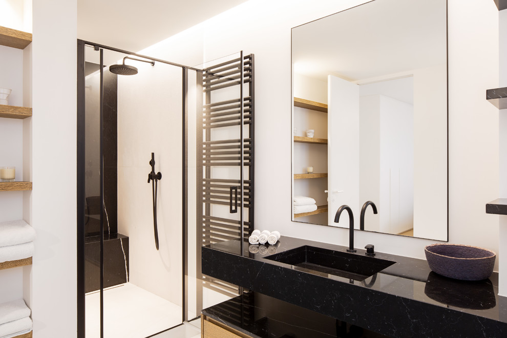 Mid-sized contemporary master bathroom in Paris with flat-panel cabinets, medium wood cabinets, a curbless shower, a wall-mount toilet, white tile, ceramic tile, white walls, ceramic floors, an undermount sink, marble benchtops, white floor, a hinged shower door and black benchtops.