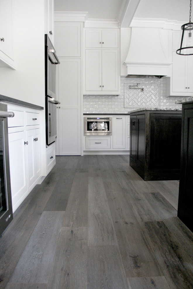 Eat-in kitchen - large single-wall light wood floor and brown floor eat-in kitchen idea with an undermount sink, recessed-panel cabinets, white cabinets, granite countertops, white backsplash, subway tile backsplash, stainless steel appliances and an island