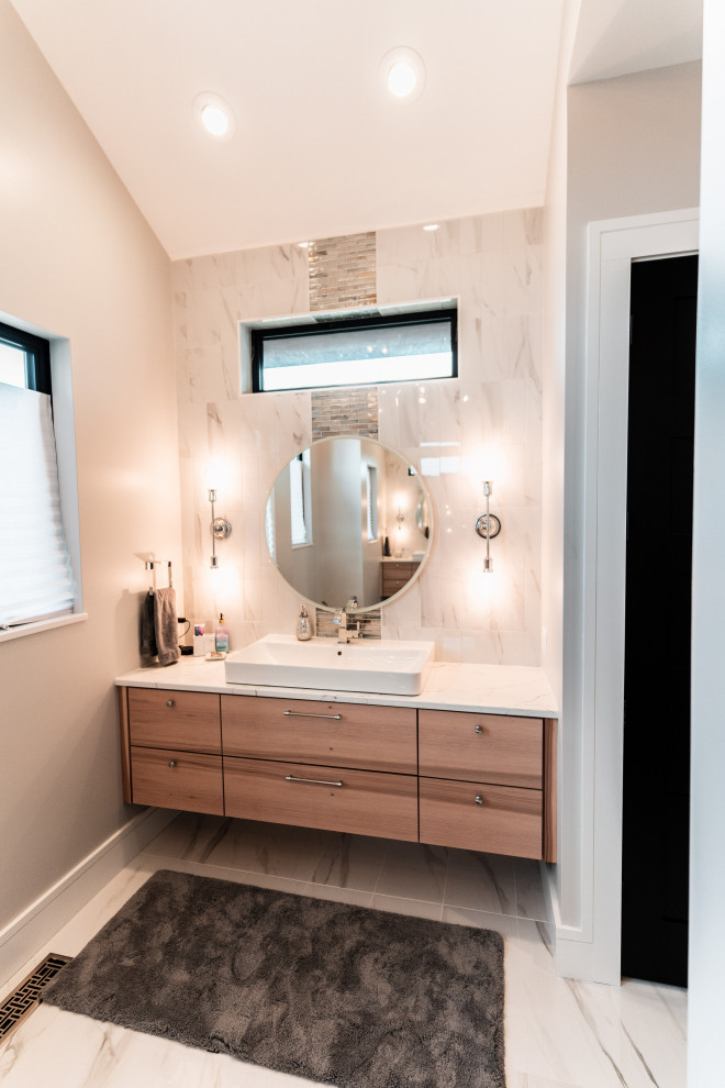 На фото: большая главная ванная комната в современном стиле с плоскими фасадами, светлыми деревянными фасадами, накладной ванной, двойным душем, белой плиткой, керамической плиткой, серыми стенами, полом из керамогранита, настольной раковиной, столешницей из искусственного кварца, разноцветным полом, душем с распашными дверями, белой столешницей, тумбой под одну раковину и подвесной тумбой с