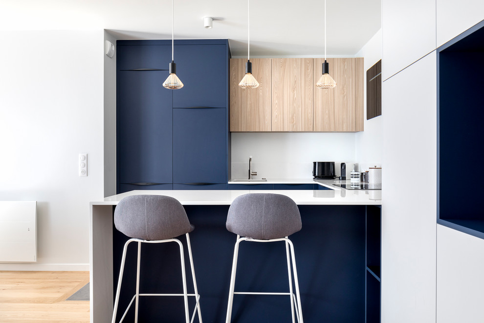 Inspiration for a mid-sized beach style u-shaped open plan kitchen in Paris with a single-bowl sink, flat-panel cabinets, blue cabinets, solid surface benchtops, white splashback, light hardwood floors, white benchtop, a peninsula and beige floor.